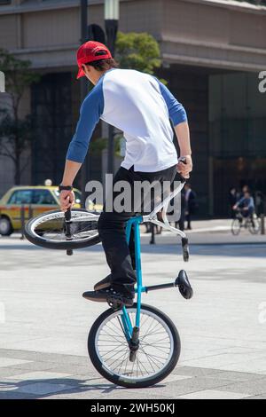 Un pilota giapponese BMX esegue trucchi in una piazza pubblica nel mezzo dell'area commerciale di Tokyo, in Giappone. Foto Stock