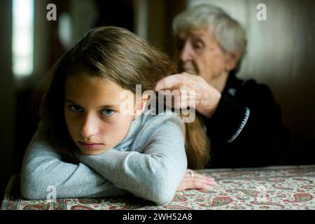 Una nonna treccia i capelli della sua frustrata nipote. Foto Stock