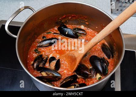 Una pentola di cozze fresche cucinate in una vivace salsa di pomodoro e aglio, condita con erbe aromatiche, perfetta per una festa a base di pesce. Foto Stock