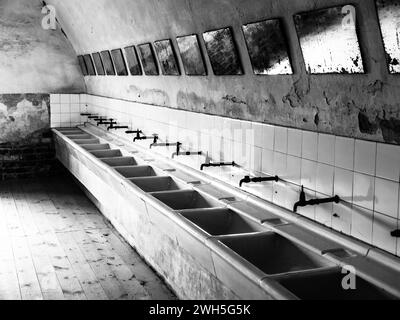 Fila di lavandini e specchi nel vecchio bagno della prigione, immagine in bianco e nero Foto Stock