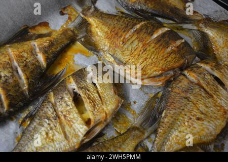 Pesce delizioso e sano, al forno, Carassius con limone su una teglia nera da forno con carta bianca pergamena. Foto Stock