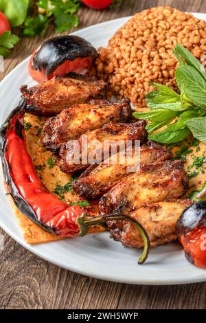 Ali di pollo alla griglia guarnite con bulgur pilaf, peperoni arrostiti e pomodori. Ali di pollo tradizionali turche Foto Stock