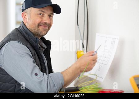 elettricista maschio che controlla la tensione della presa con il multimetro in sede Foto Stock