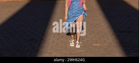 Bella giovane donna amputata in un abito che cammina nel parco durante il giorno di sole. La vita va avanti in ogni caso. Foto Stock