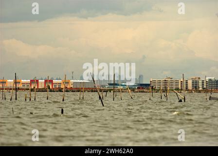 Una vista dall'acqua costiera di Bekasi appena prima del confine con Giacarta, Indonesia. La nuova area commerciale chiamata Marunda Makmur sull'estuario del canale alluvionale di Giacarta (a sinistra) e i nuovi edifici pianeggianti nel villaggio Marunda di Giacarta (a destra) sono fotografati sullo sfondo di alcuni degli edifici torreggianti della capitale. Foto Stock