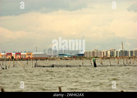 Una vista dall'acqua costiera di Bekasi appena prima del confine con Giacarta, Indonesia. La nuova area commerciale chiamata Marunda Makmur sull'estuario del canale alluvionale di Giacarta (a sinistra) e i nuovi edifici pianeggianti nel villaggio Marunda di Giacarta (a destra) sono fotografati sullo sfondo di alcuni degli edifici torreggianti della capitale. Foto Stock