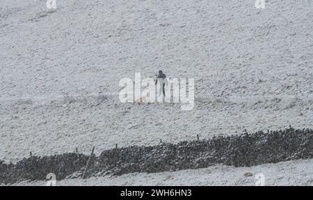 Hope Valley, Peak District, Derbyshire, 8 febbraio 2024. Un Dog Walker affronta la neve pesante questa mattina nella Hope Valley. Crediti: Michael Jamison/Alamy Live News Foto Stock