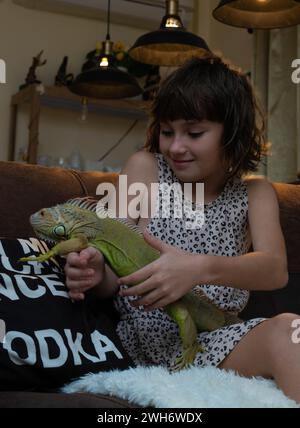 Bambino che gioca con una grande iguana verde in salotto Foto Stock