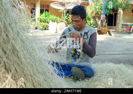 Lampung, Indonesia, 16 ottobre 2022: Pescatori commerciali riparano o ricamano reti danneggiate in una zona di essiccazione. Concetto di stile di vita di etnia indigena Foto Stock