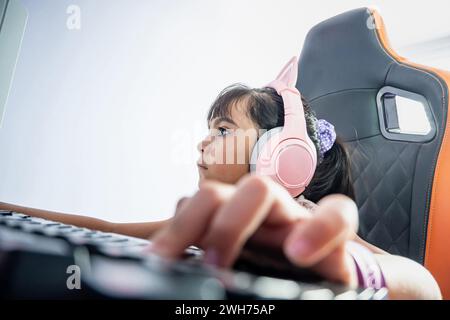 Una ragazzina latina che gioca. È concentrata a giocare online. Indossa le cuffie e siede su una sedia da gioco. Foto Stock