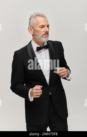 attraente uomo maturo con barba in smoking nero con fiocco che posa in movimento mentre balla Foto Stock