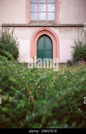 Una porta verde della chiesa ad arco gotica incorniciata in pietra rosa vista su una siepe; la chiesa di Santo Stefano, Magonza. Foto Stock