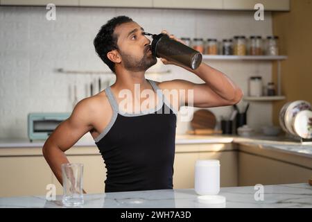 Felice uomo in forma di mezza età che beve frullato proteico dal biberon in cucina dopo l'allenamento mattutino - concetto di supplemento muscolare e resistenza o corpo Foto Stock