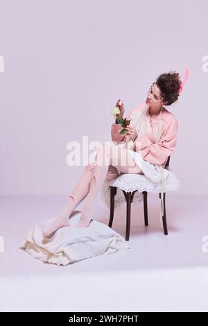 Bella giovane donna seduta su una sedia e dipinge fiori di rosa bianchi con smalto rosso. Rendere la vita più luminosa, dare più passione. Foto Stock