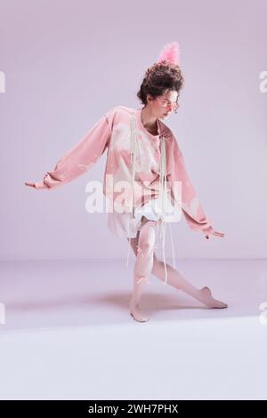 Bella giovane donna con vestiti accoglienti e graziosi che ballano come ballerina di nuovo sfondo rosa pastello. Hobby, estetica Foto Stock