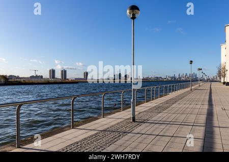 Lungo il fiume Tamigi, nella zona est di Londra, si trova un'ampia passerella di fronte all'aeroporto di London City. Bel tempo soleggiato con cieli azzurri e luci stradali. Foto Stock