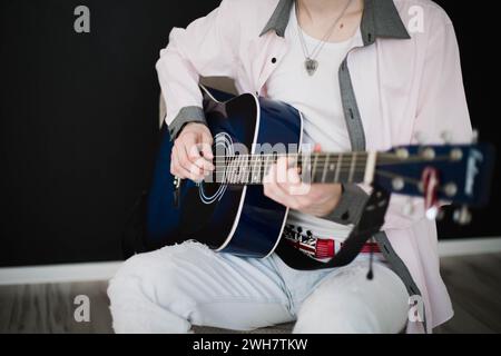 Un giovane uomo sottile e attraente in camicia bianca che suona la chitarra blu su sfondo nero, primo piano Foto Stock