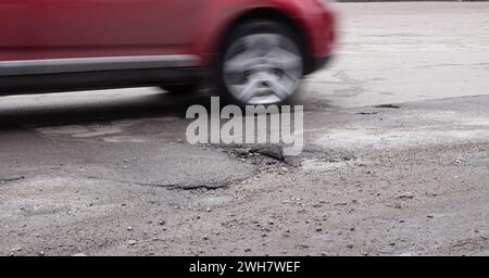 La macchina gira intorno a una buca sulla strada. Asfalto rotto dopo l'inverno. Riparazione stradale. Foto Stock