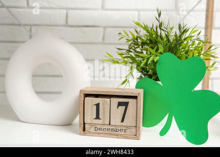 Ripiano bianco con foglio di carta, calendario a cubetti e arredamento in soggiorno, primo piano. St Festa di Patrick Foto Stock