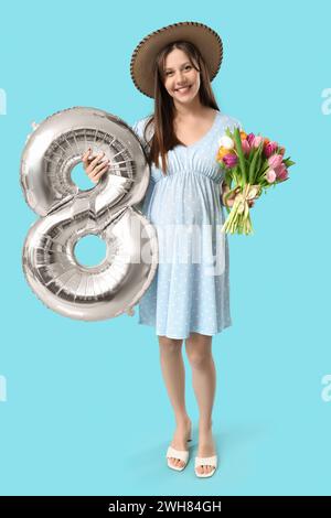 Bella giovane donna incinta con bouquet di tulipani e pallone aerostatico argentato a forma di figura 8 su sfondo blu. Giornata internazionale della donna Foto Stock