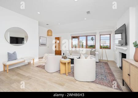 Soggiorno moderno con mobili bianchi e pavimenti in legno duro, dotato di un elegante televisore a schermo piatto Foto Stock