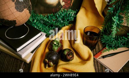 STILL Life allestito su un tavolo di legno con tre frutti di mangostano viola, replica di dipinti classici, pila di libri, finte viti verdi, penna per immersione, notebook, y Foto Stock