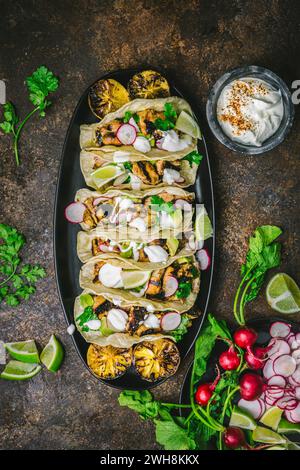 Disposizione di Tacos di pollo alla griglia su un piatto scuro con ravanelli affettati, limes, coriandolo, limoni affumicati e panna acida Foto Stock