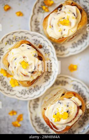 Tre involtini di limone ricoperti di glassa di formaggio spalmabile, presentati su piatti e guarniti con fiori gialli. Foto Stock