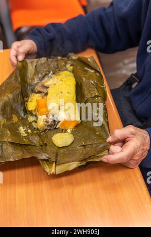 Le mani di una donna aprendo un tamale colombiano su un tavolo Foto Stock