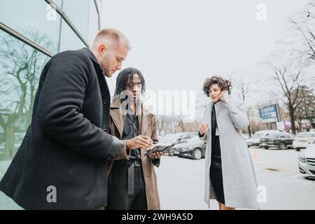 Un gruppo multiculturale di professionisti aziendali riuniti all'esterno, che collaborano rivedendo i contenuti su un tablet digitale con una persona durante una chiamata. Foto Stock