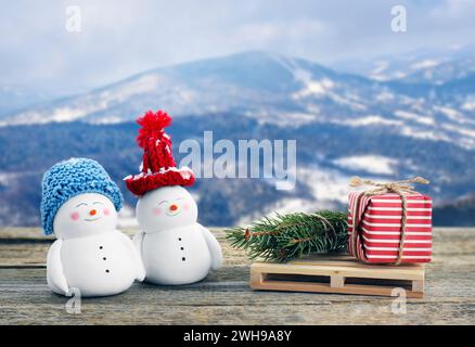 Simpatici pupazzi di neve decorativi, confezione regalo e rami di abete su un tavolo di legno in montagna Foto Stock