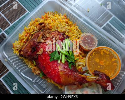 Vista dall'alto del riso arabo con cosce di pollo rosso, riso colorato e zuppa di curry in un contenitore di plastica bianco. Foto Stock