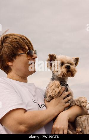 Santander, Spagna. 7 luglio 2023 donna sorridente felice che tiene in braccio il cane terrier dello Yorkshire. Persone con animali domestici canini, adorabili cuccioli all'aperto. Foto verticale Foto Stock