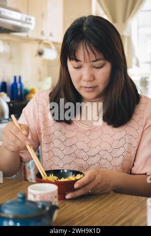 Primo piano della giovane donna asiatica mangia riso con bacchette a casa Foto Stock