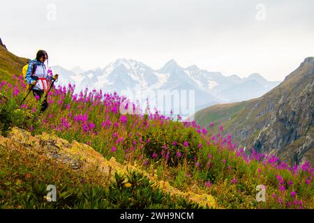 Vista laterale che segue una donna sportiva escursionista con bastoncini da nordic Walk sul punto panoramico in salita nel sentiero escursionistico verde delle montagne del caucaso. Attivit ricreative Foto Stock