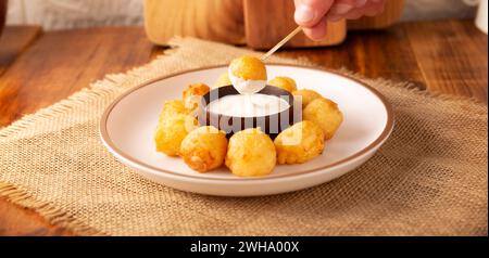 Mano umana che immerge un bocconcino di formaggio impanato fritto, una ricetta di spuntini fatti in casa facile e deliziosa. Servito con salsa per immersione. Foto Stock