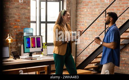 Giovane donna caucasica e giovane uomo asiatico chiacchierano in un ufficio moderno con un'atmosfera informale di lavoro Foto Stock