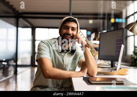 Il giovane asiatico sorride alla sua scrivania in ufficio, vestito per affari informali Foto Stock