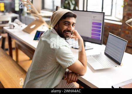 L'uomo asiatico in un abbigliamento casual sorride in ufficio, suggerendo un'atmosfera creativa. Foto Stock