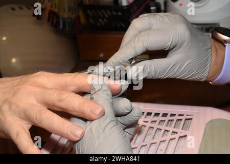 La foto mostra le mani di un manicurista e di un cliente. Un manicurista utilizza delle pinze per rimuovere le cuticole dalle unghie. Foto Stock