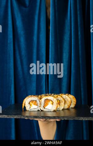 Cibo popolare. Panini di sushi serviti a bordo su uno sfondo blu profondo con una tenda blu. Menu del ristorante asiatico Foto Stock