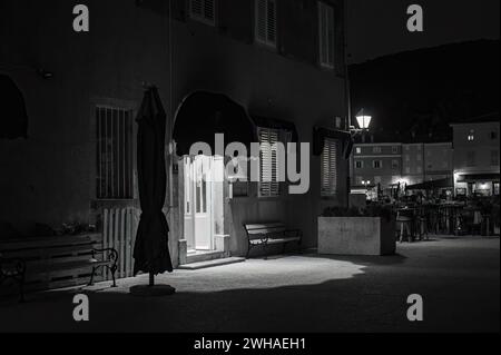 Cherso, Croazia - 24 ottobre 2022: Stretta strada di Cherso di notte, ingresso a una casa, bianco e nero Foto Stock