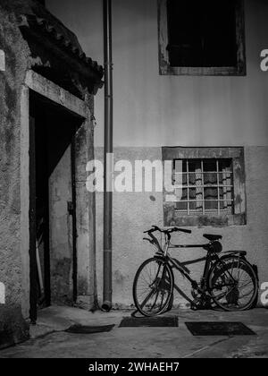 Cherso, Croazia - 24 ottobre 2022: Stretta via di Cherso di notte, vecchia bicicletta, bianco e nero Foto Stock