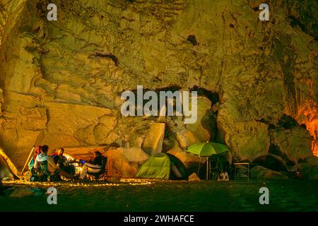 Campeggiatori sotto cieli stellati con tende e luci da campeggio, annidati dal mare e da una montagna rocciosa, creando un ambiente di campeggio costiero sereno Foto Stock