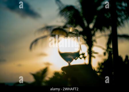 Un momento accattivante sorseggiando un bicchiere da cocktail al tramonto delle Maldive, mescolando sapori esotici con la tranquilla bellezza del paradiso costiero. Foto Stock