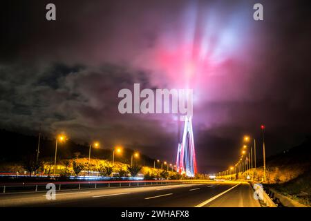 Il Ponte sul Bosforo di notte, adornato da vivaci luci rosse che si riflettono sulle nuvole, creando un paesaggio urbano drammatico e colorato sopra Istanbul Foto Stock