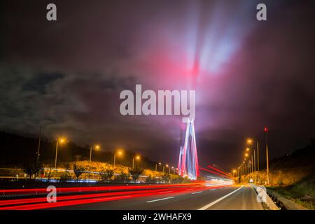 Il Ponte sul Bosforo di notte, adornato da vivaci luci rosse che si riflettono sulle nuvole, creando un paesaggio urbano drammatico e colorato sopra Istanbul Foto Stock