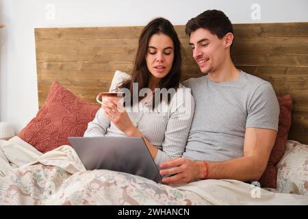 Coppia spagnola che usa il portatile e beve caffè a letto. Foto Stock