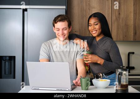 Coppia multietnica sorridente, che utilizza il laptop mentre fa colazione. Foto Stock