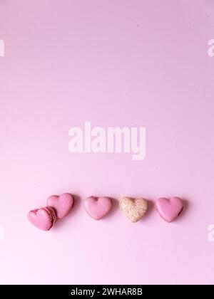 cinque biscotti al macaron rosa a forma di cuore su sfondo rosa Foto Stock